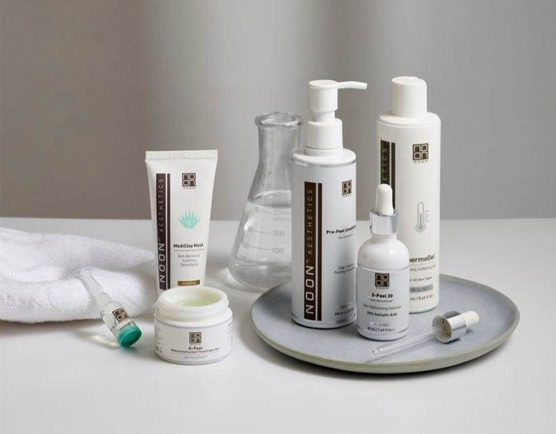 Noon Aesthetics huidverzorgingsproducten op schaal met pipet en handdoek, geschikt voor professionele gezichtsbehandelingen.