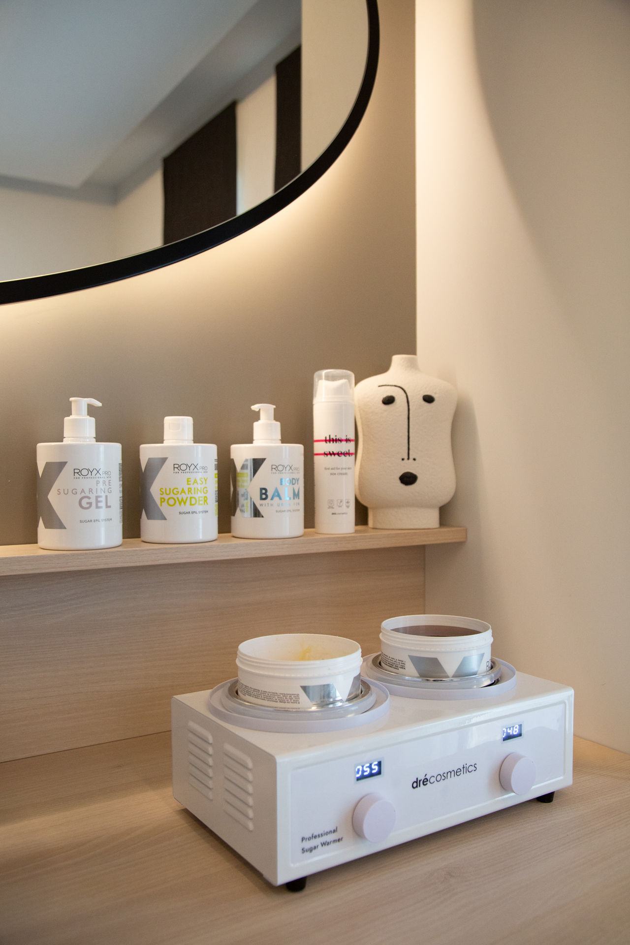 Royx Pro producten voor suikerontharing in salon, met sugaring gel, sugaring powder en body balm op een plank naast een professionele suikerwarmer.